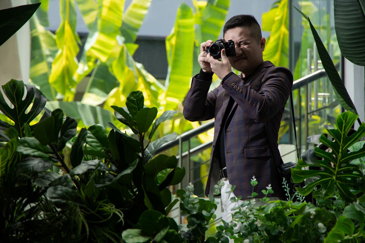 Kevin Lee raising his camera to take a photograph, tropical plants behind