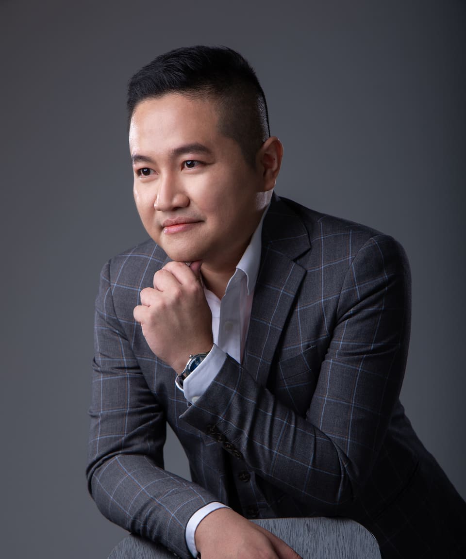 Portrait of Kevin Lee: grey background, chin resting on his hand, smiling